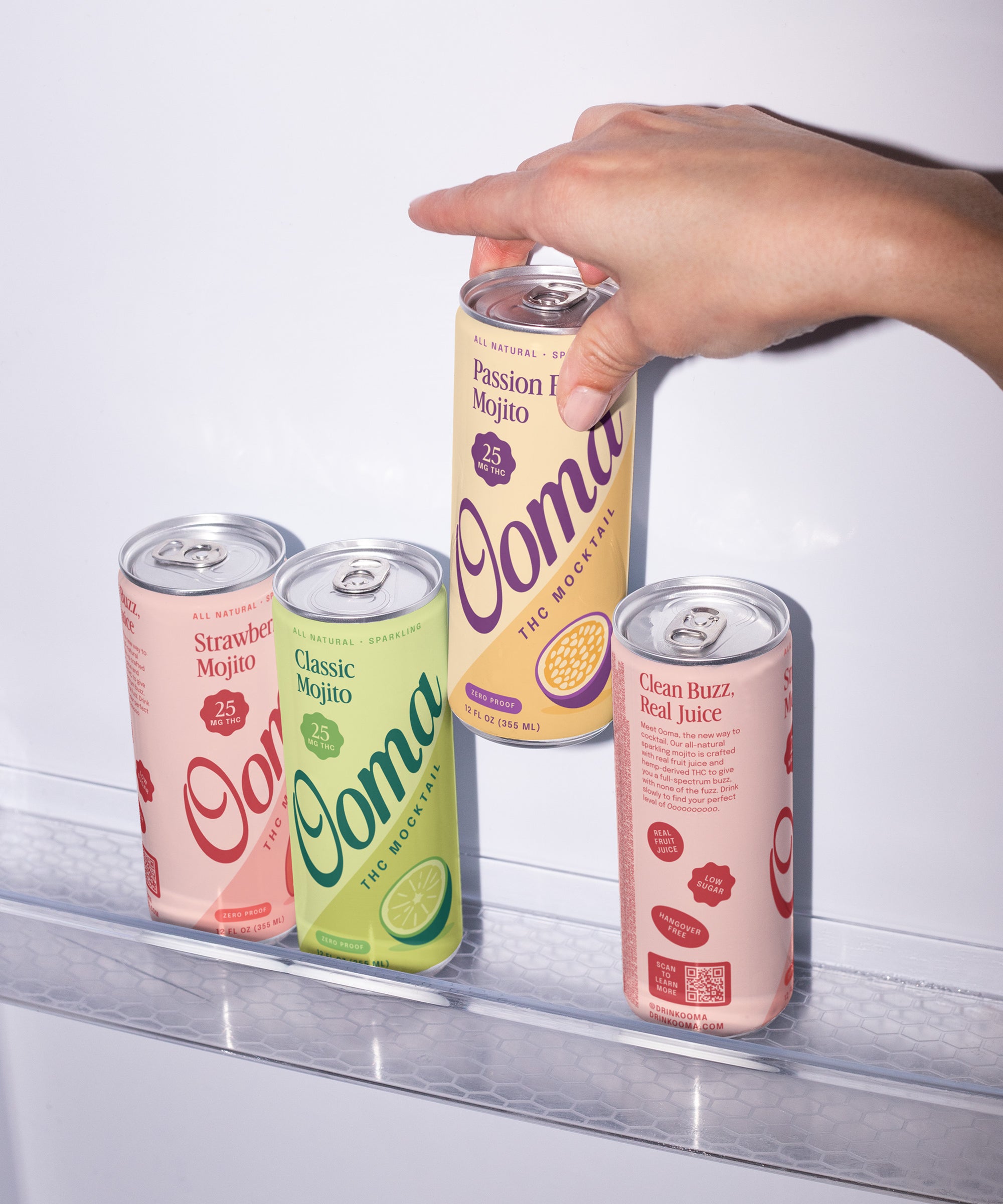 Hand reaching for a can of Ooma Passion Fruit mojito in a refrigerator with other Ooma cans on shelf.